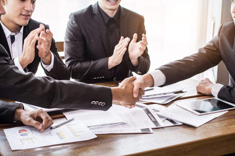 Businessmen shaking hands in front of other colleagues.
