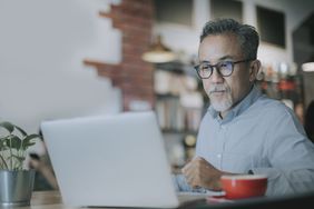 Older person working at a computer with a red coffee cup in front of him