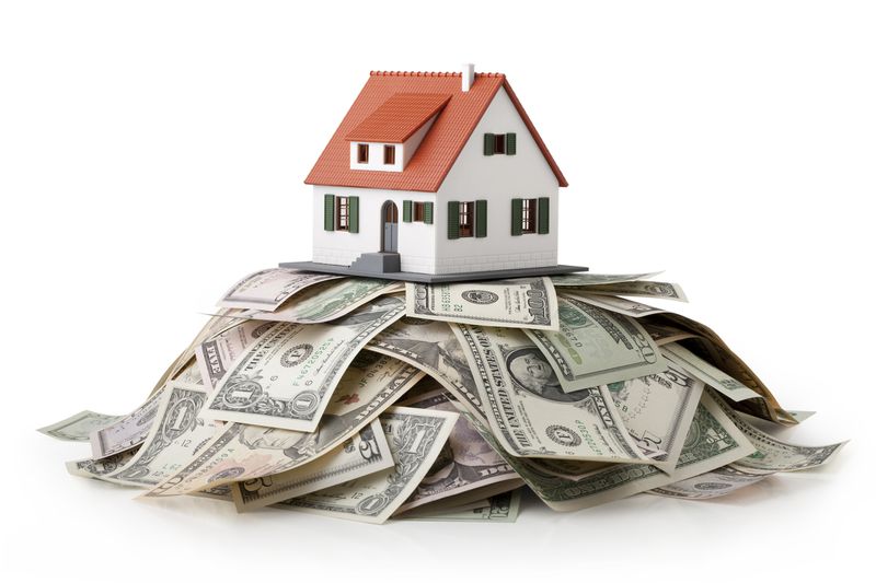 A miniature model house standing on a heap of dollar bills.