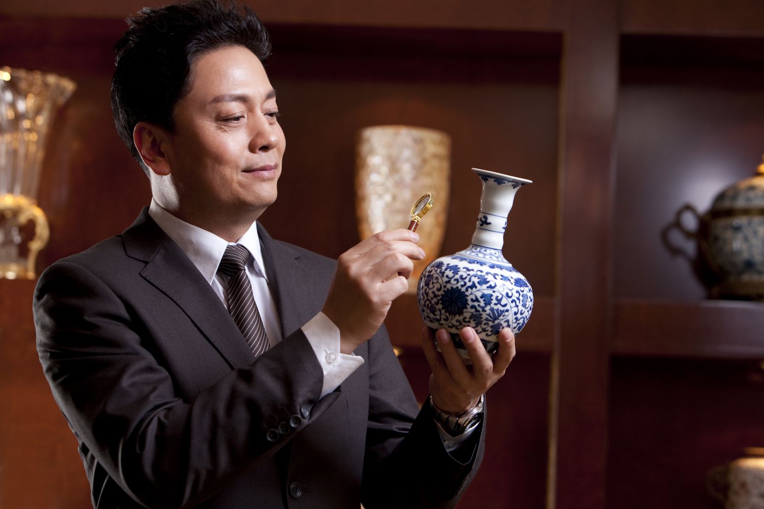 Man in a suit looks at antique vase through a magnifying glass