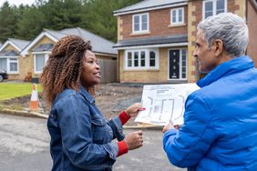 Waist-up rear-view shot of two people looking over real estate plans at a housing development site.