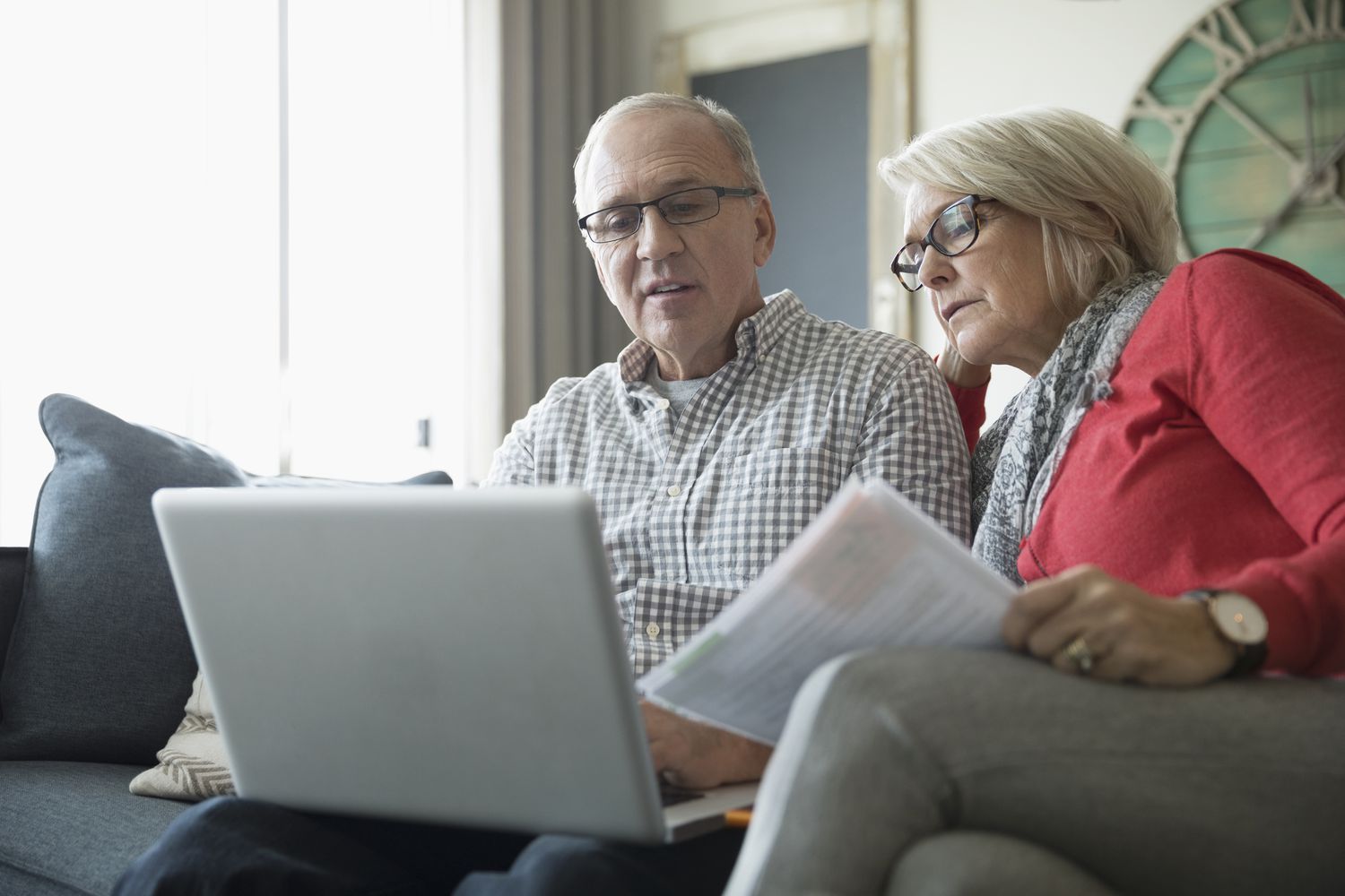 Older couple at a laptop and holding papers.