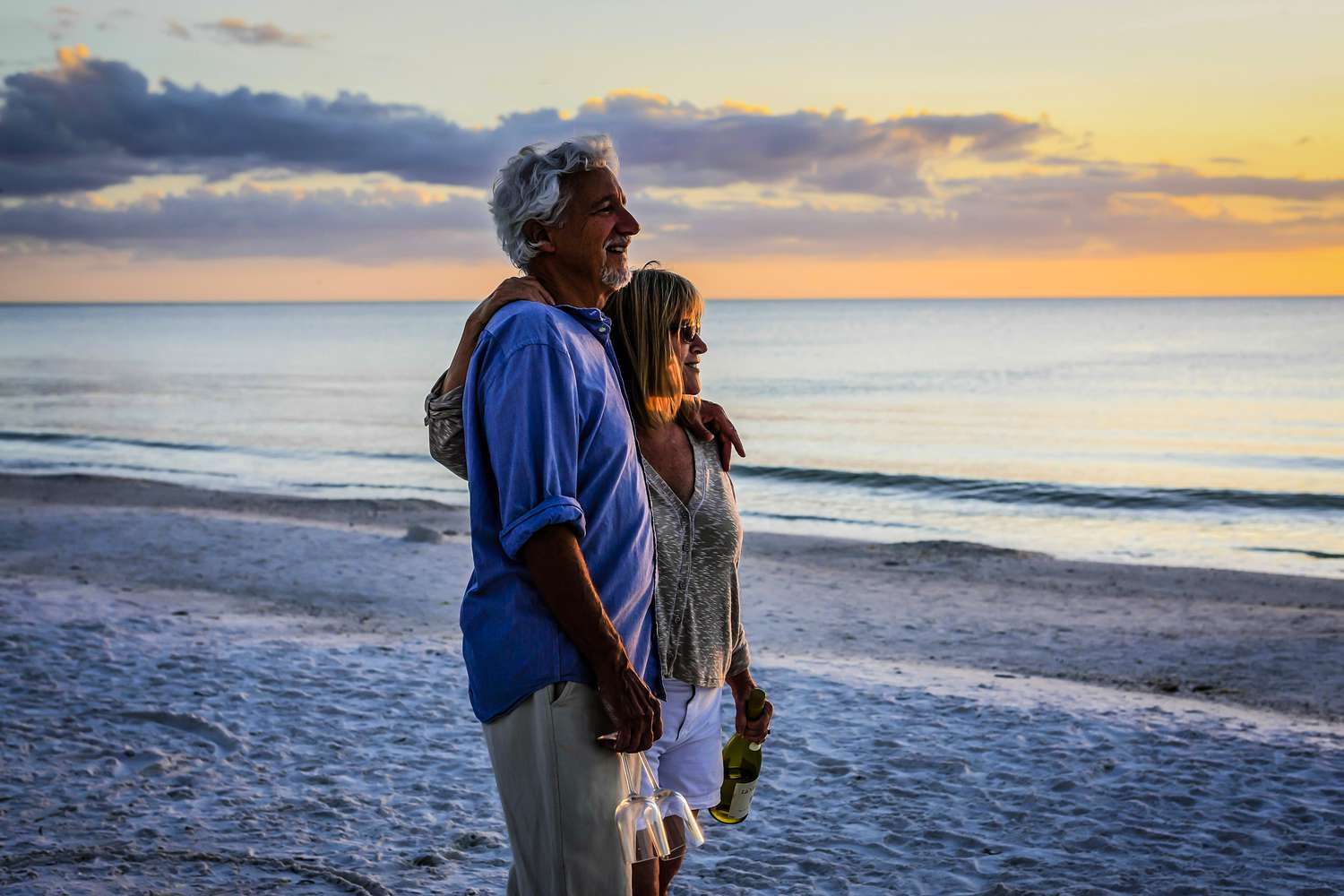 Retired couple enjoy a romantic interlude with a bottle of wine and two glasses at sunset on Siesta Key beach Florida.