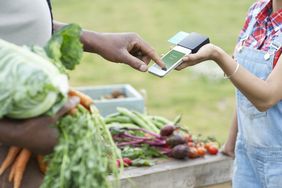 A man pays a woman for some vegetables using a mobile payment device.
