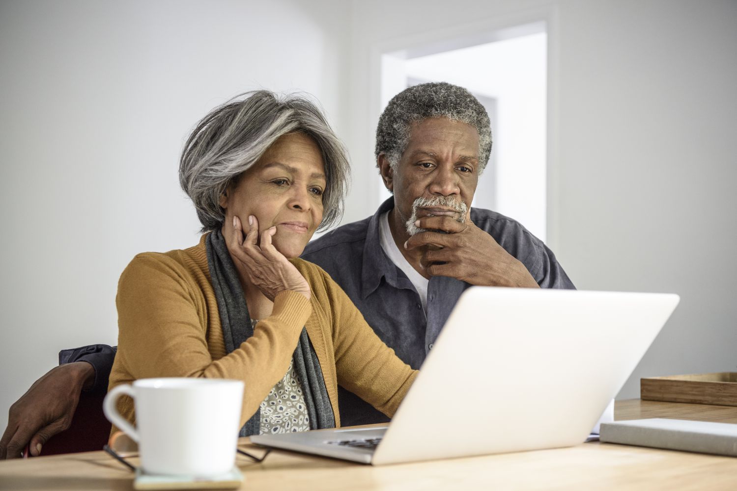 Older couple sitting together at their kitchen table and pondering something on their laptop