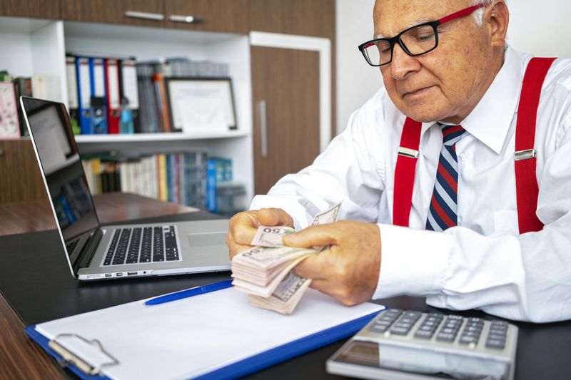 A man with red glasses counting money sitting at the desk.