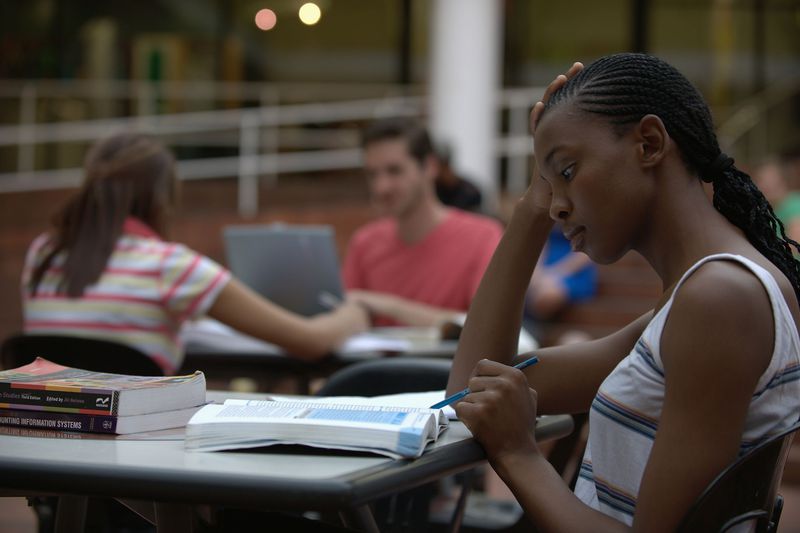 Female student studying with textbook with other students working at desks behind her.