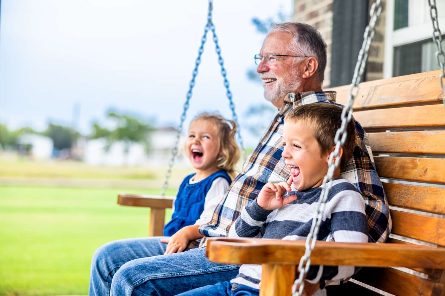 Grandpa making the grandkids laugh while they sit on a porch swing together.