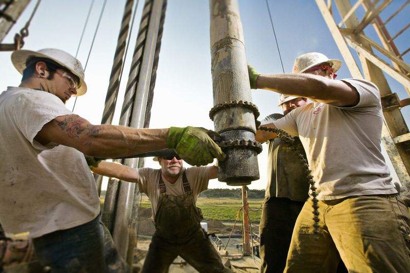 Oil Workers Using Chain to Position Drill on Drilling Platform