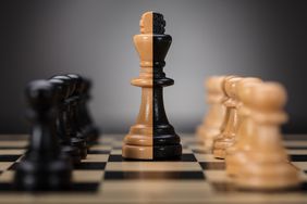 Black- and brown-colored king and pawns on chess board.
