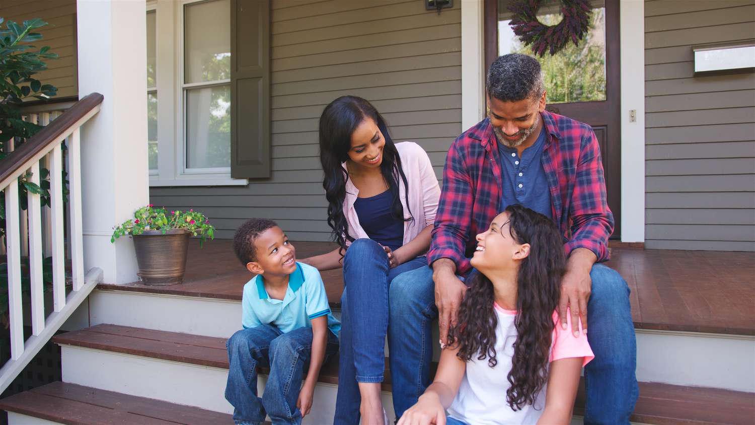 Portrait Of Smiling Family Sitting On Steps Of Suburban Home