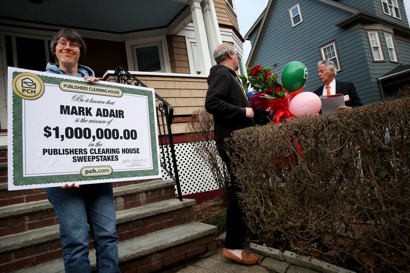 Sara Adair shows off the oversized check for $1 million that her husband received from Dave Sayer of the Publishers Clearing House Prize Patrol in South Boston, Mass., in 2022 