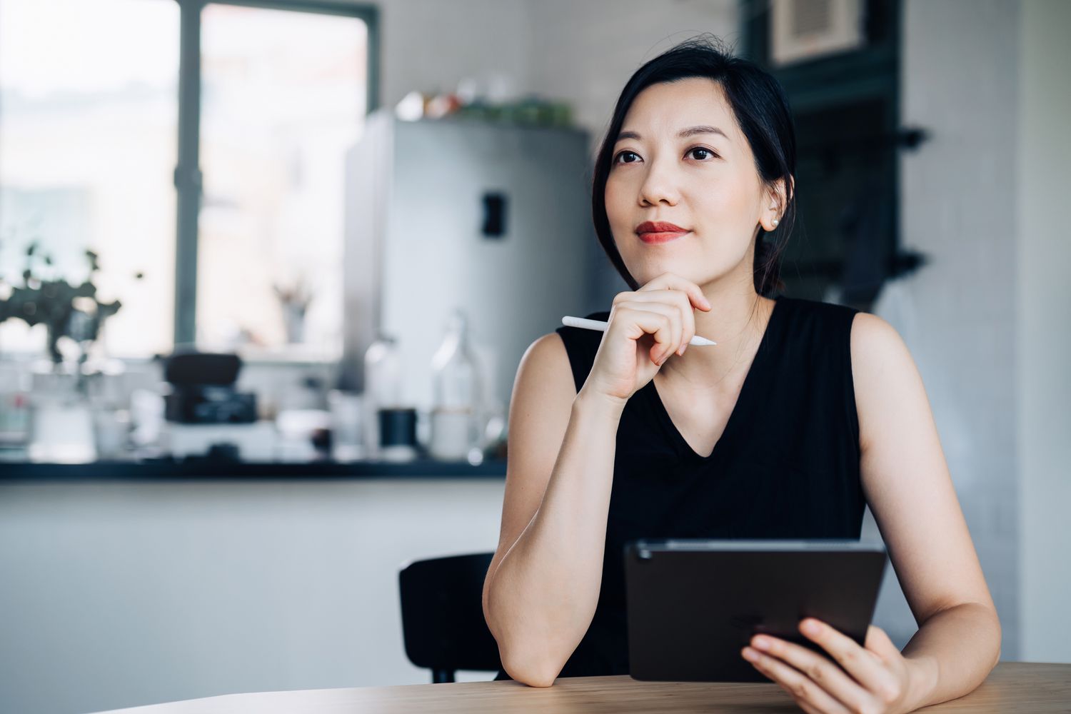 Thoughtful young Asian woman handling personal banking and finance with digital tablet at home.
