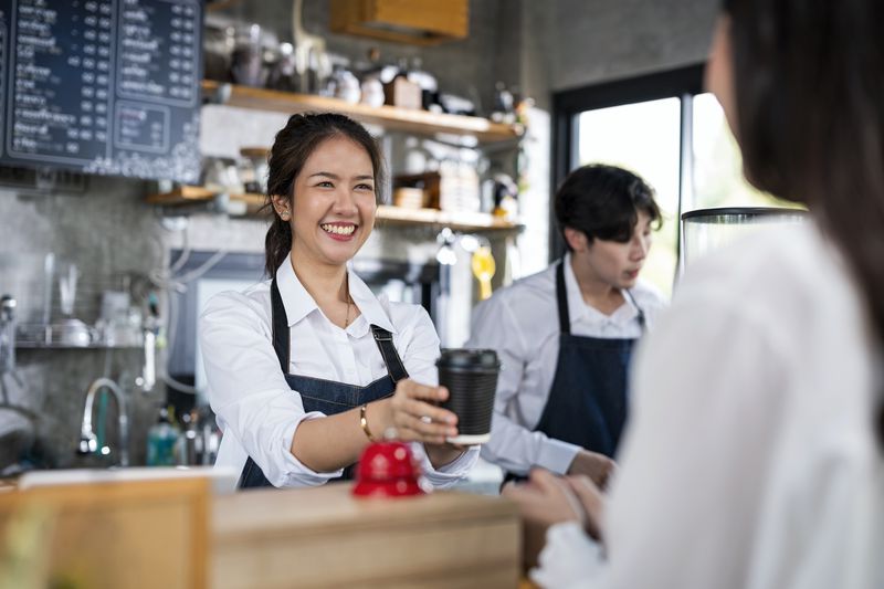 An hourly worker hands a coffee to a customer.