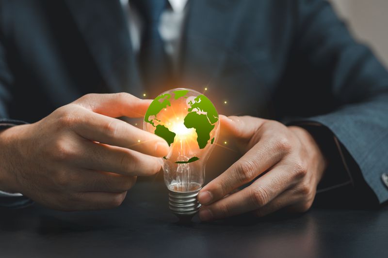 A businessperson holds a light bulb featuring a green Earth to represent sustainability and environmental responsibility in the modern world.