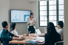 A woman presents charts to a group of four people in an office