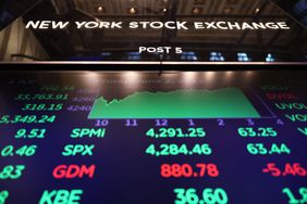 Stock market numbers are displayed in red and green on a screen at the New York Stock Exchange