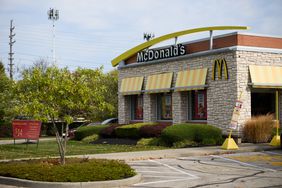 A McDonald's restaurant is seen next to green grass, trees, and bushes.