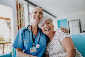 Healthcare professional hugging senior patient while both smiling happily.