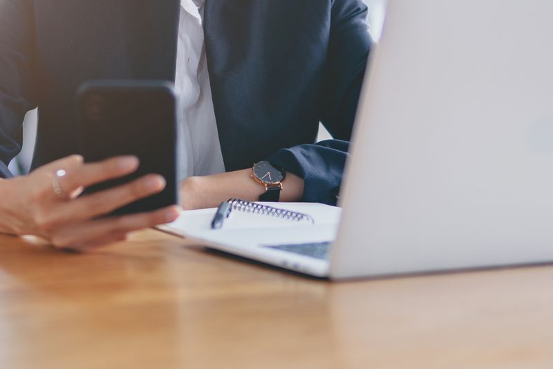 A businesswoman checking her phone and using a laptop.