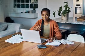 A woman reviews papers and works on a laptop at a table.