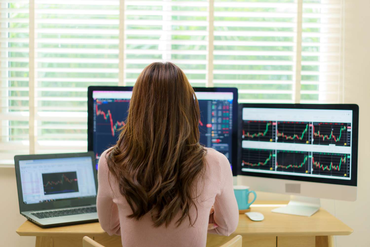 Woman trader at work in home office looking at charts on several monitors