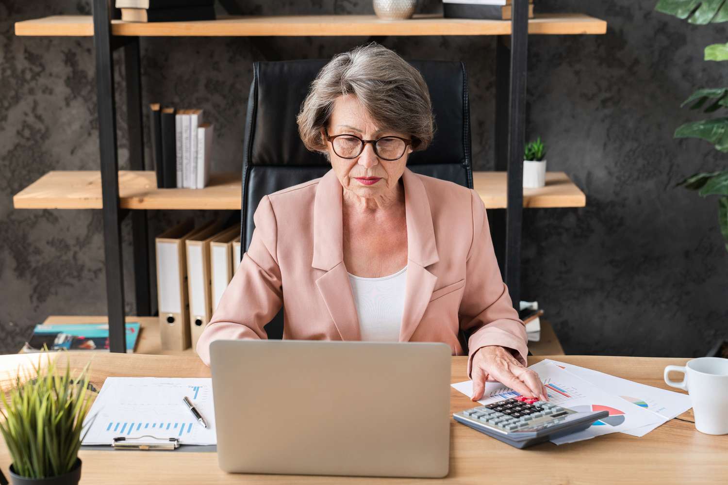 An older woman working at a desk with a laptop and calculator