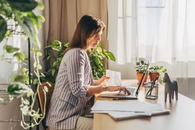 Woman at a desk near a window with a laptop and paperwork. 