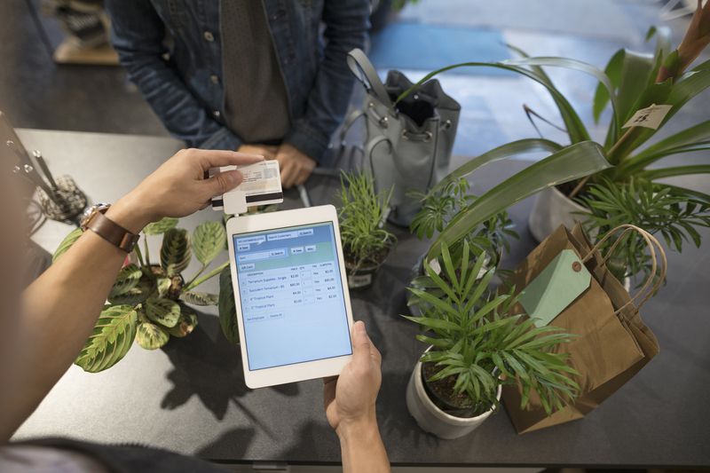Cashier swiping digital tablet credit card payment in plant shop.