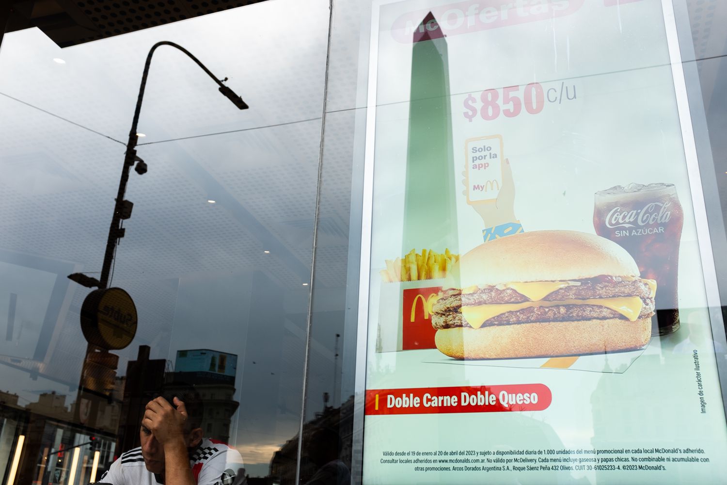 A man sits inside a fast food chain restaurant as the Obelisk is reflected on the window with the sign of meal price on March 15, 2023 in Buenos Aires, Argentina.