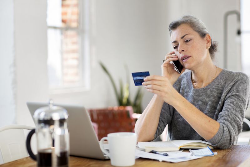 Woman holding credit card talking about its statement on the phone