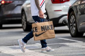 A person crosses the street wearing Nike shoes and carrying a Nike bag. 