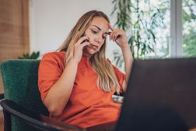 Distressed woman sitting down on phone with computer on lap