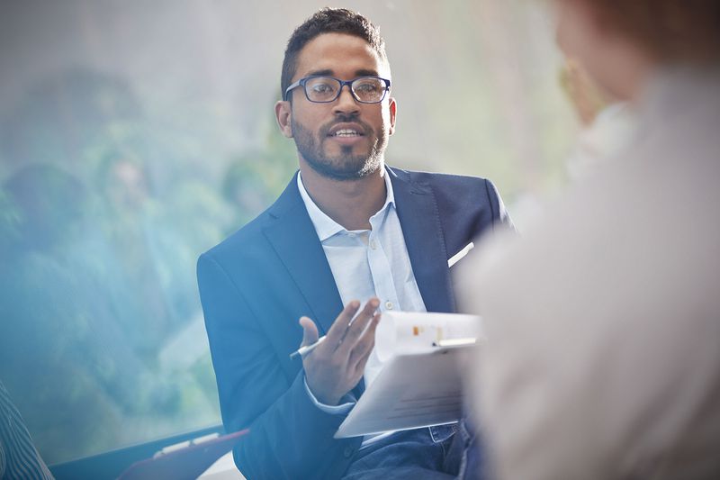 Man With Clipboard Talking in Meeting