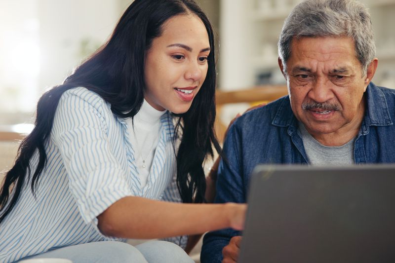 Person with long dark hair and their older parent work on a student financial aid application on a laptop computer.