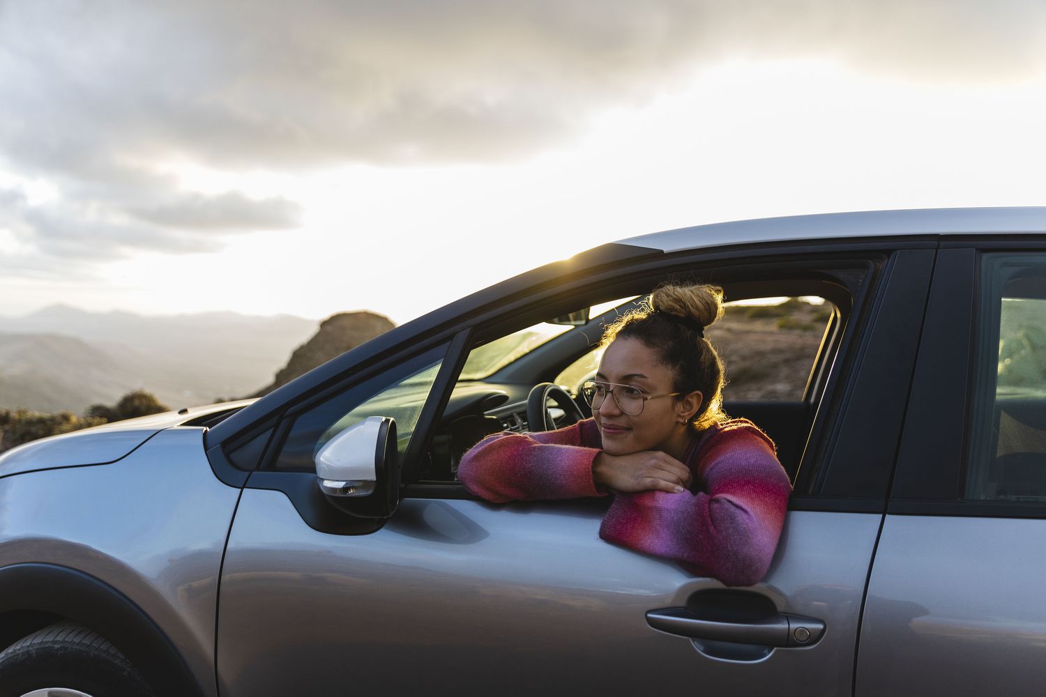 Smiling woman leaning out of car window at sunset