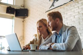 Young couple sitting in a coffee shop and looking together at mortgage rates on a laptop