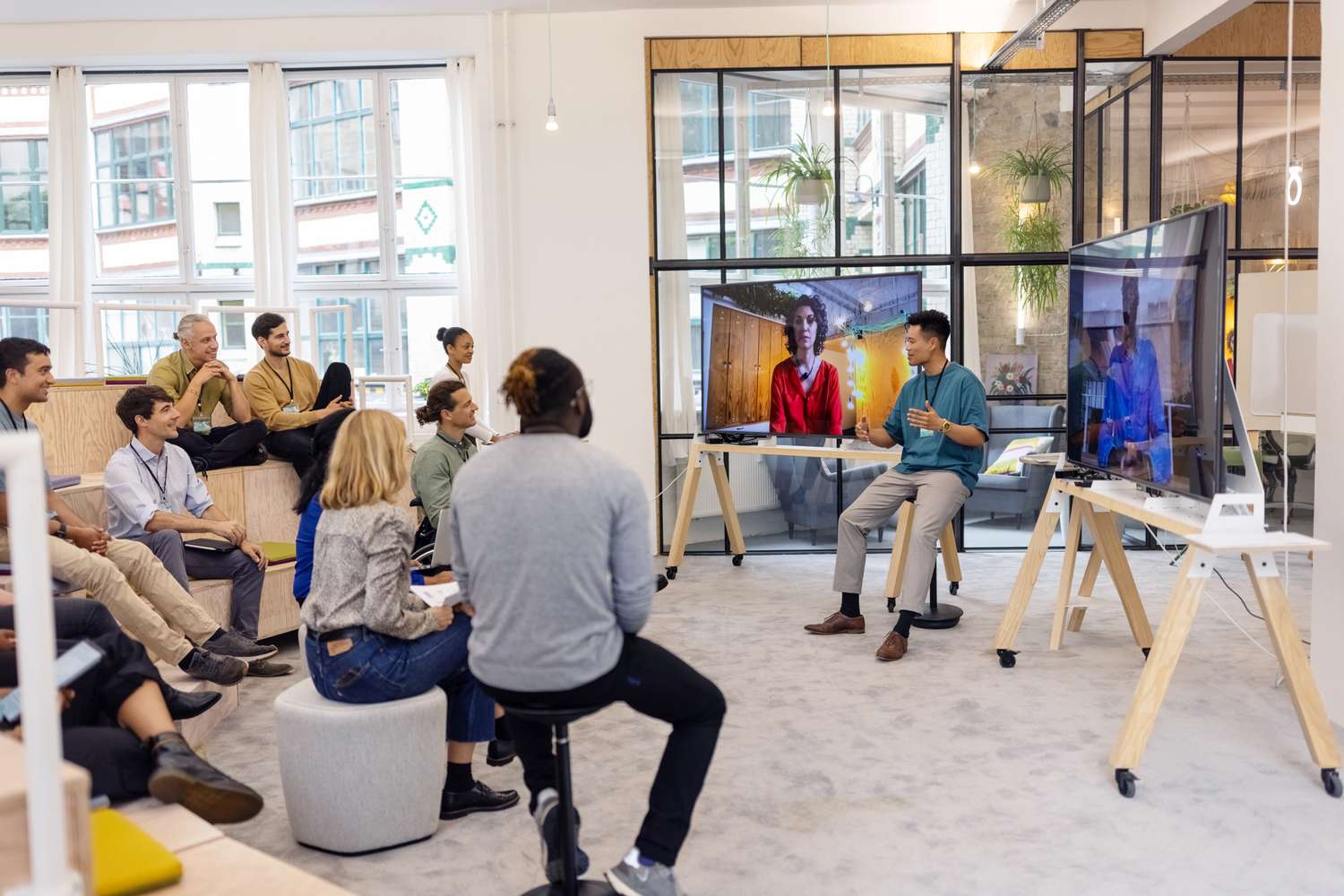 A group of co-workers attending a team meeting in person and virtually discuss company networking within the corporate structure.