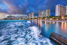 Waves surge toward Waikiki’s beaches in the blue hour in Honolulu, Hawaii.