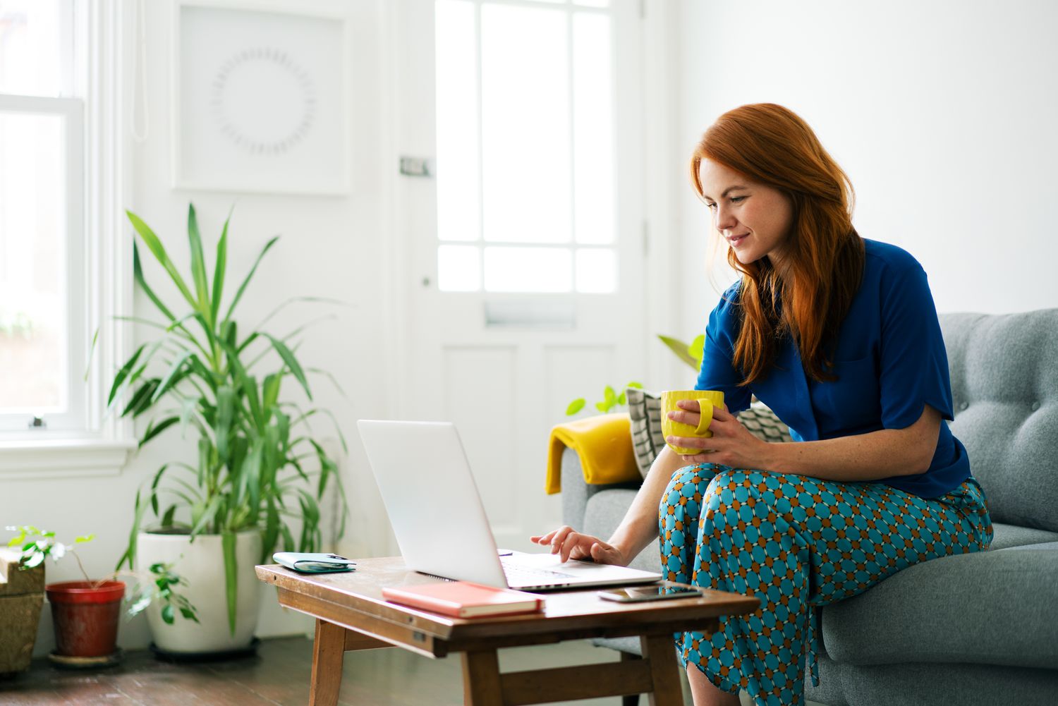 A woman sits on her couch looking at her laptop on the coffee table