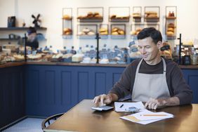 Mature man owner staff employee using calculator for sales analysis accounting bookkeeping in small business bakery cafe