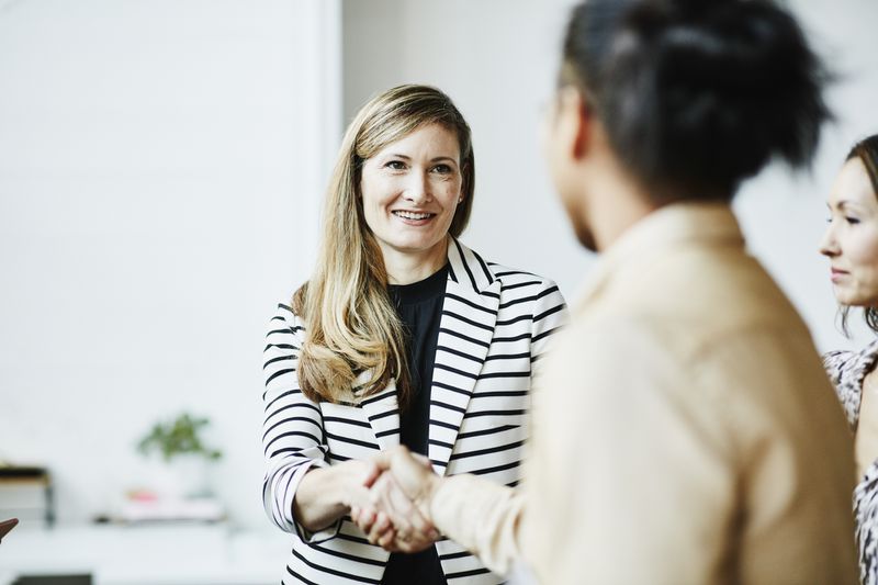 Two people shake hands in an office setting.