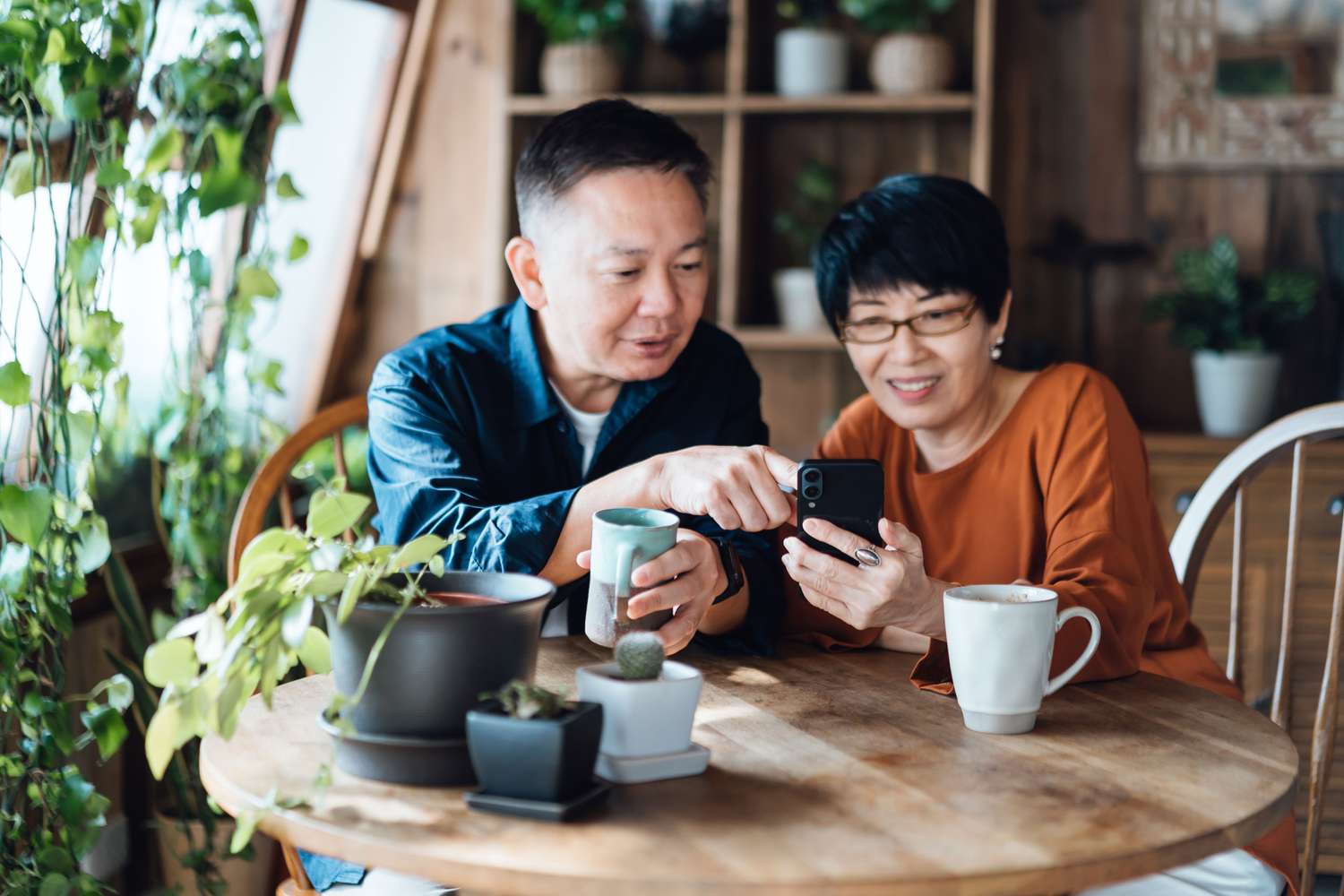 Two people seated at a home table, reviewing information on a smartphone screen