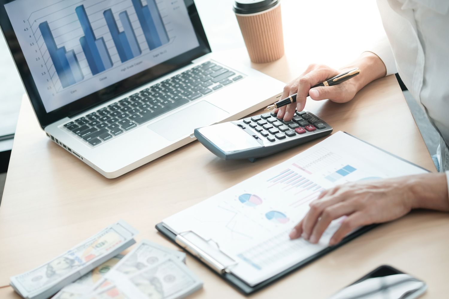 A midsection of a person analyzing charts with a calculator and a laptop on office desk.