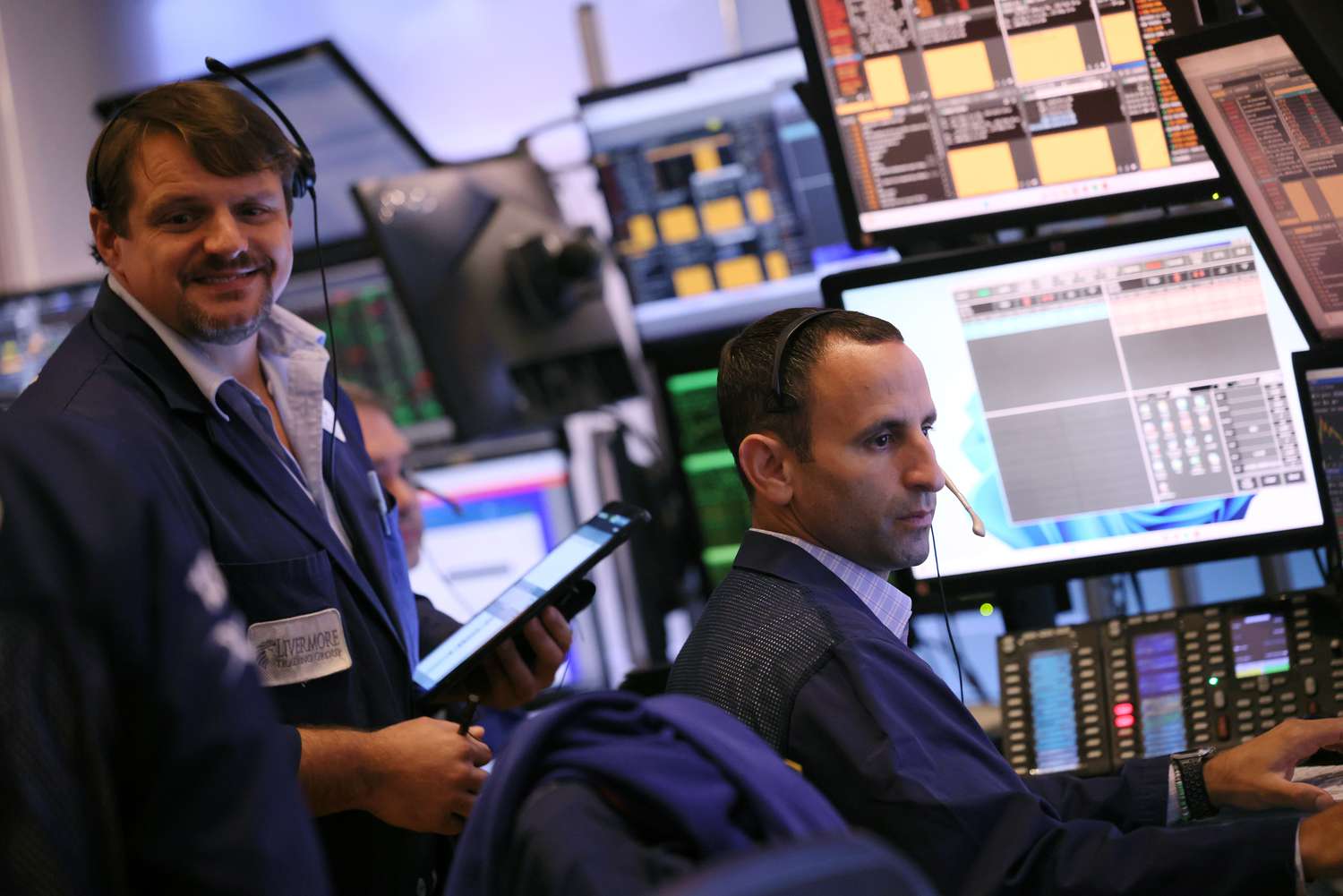 Two traders wearing headsets work on the floor of the New York Stock Exchange, surrounding by computer screens. 