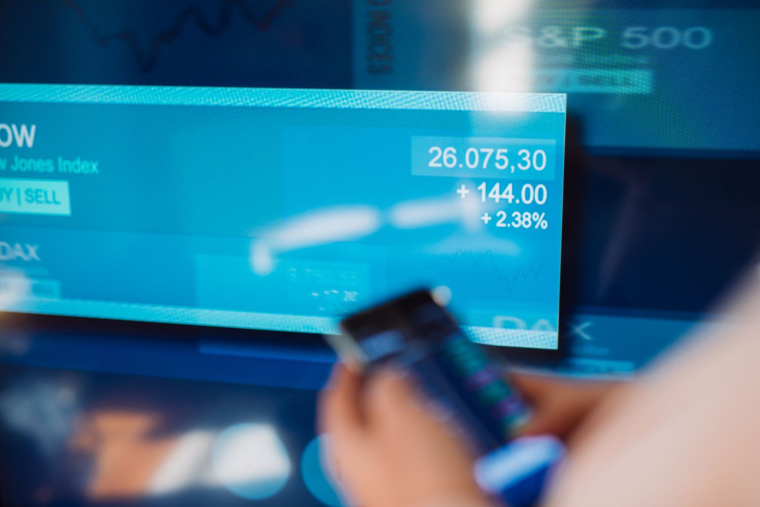 Person trading stock with mobile app in front of stock exchange screen.