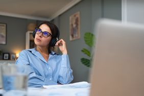 Woman sitting in home office looking up and to the right reflectively.