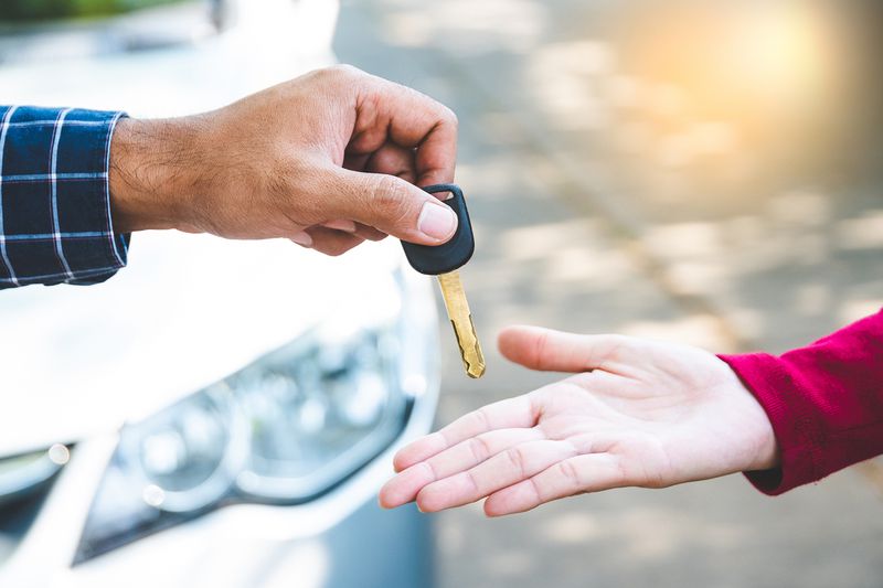 Close up hand male giving a key new car on hand female outside her car. Concept of rent car or buying car