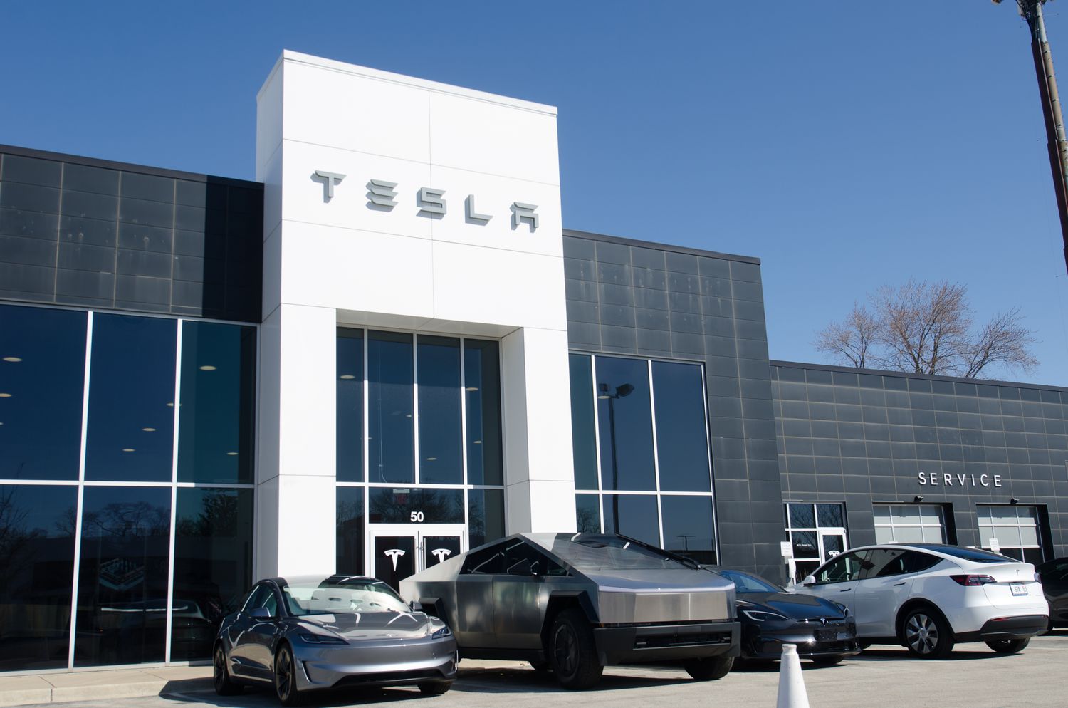 Tesla vehicles are seen in front of a black and white dealership building.