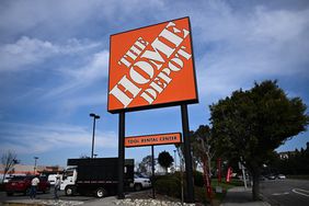 The orange Home Depot sign is seen in front of cars in a parking lot and a blue sky.